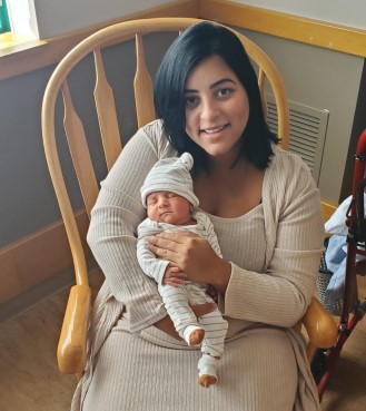 Smiling woman sitting in rocking chair holds newborn baby